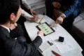 A group of professionals in suits collaborates over a tablet displaying graphs, surrounded by documents and a calculator on a table.