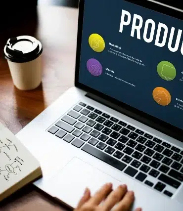 Laptop displaying a product strategy presentation with four colored icons, next to a notebook with diagrams and a coffee cup. Collaborative and focused atmosphere.