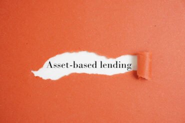 A torn orange paper reveals the phrase "Asset-based lending" in black text on a white background, evoking a theme of financial discovery.