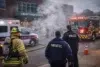 Emergency responders, including a firefighter, paramedic, and police officer, attend to a smoke-filled scene outside Liberty High School, indicating a tense situation.