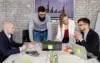 A team of four people in an office discusses charts displayed on a laptop and a screen. The mood is focused, teamwork emphasized, brick wall behind.