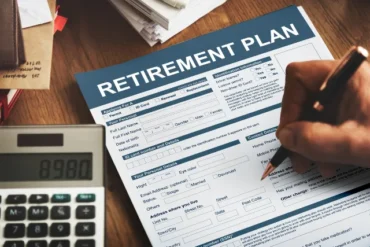 A person fills out a retirement plan form at a desk, accompanied by a calculator displaying 8980, conveying a tone of financial planning and preparation.