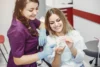 A dentist and patient are smiling and examining a dental model. The dentist, in purple scrubs, points at the model while the patient holds it.