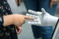 A child reaching out to touch a robotic hand, highlighting human-robot interaction in a modern setting.