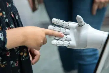 A child reaching out to touch a robotic hand, highlighting human-robot interaction in a modern setting.