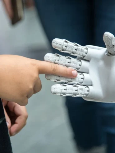 A child reaching out to touch a robotic hand, highlighting human-robot interaction in a modern setting.