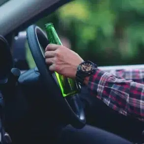 A person in a plaid shirt holds a green bottle while steering a car, suggesting the risky behavior of drinking and driving. The mood is tense.
