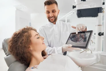 A dentist shows a smiling patient an X-ray on a tablet in a bright dental office. The atmosphere is professional and reassuring.