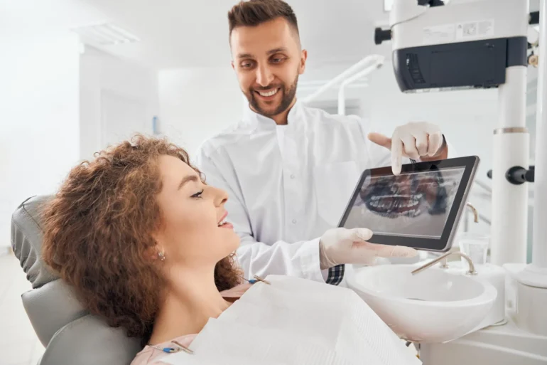 A dentist shows a smiling patient an X-ray on a tablet in a bright dental office. The atmosphere is professional and reassuring.