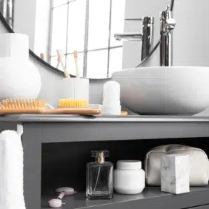 Modern bathroom with a round mirror, white sink, and a gray counter holding a toothbrush holder, comb, and toiletries. Soft, clean ambience.
