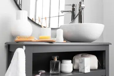 Modern bathroom with a round mirror, white sink, and a gray counter holding a toothbrush holder, comb, and toiletries. Soft, clean ambience.