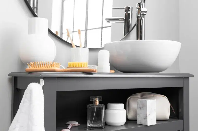 Modern bathroom with a round mirror, white sink, and a gray counter holding a toothbrush holder, comb, and toiletries. Soft, clean ambience.