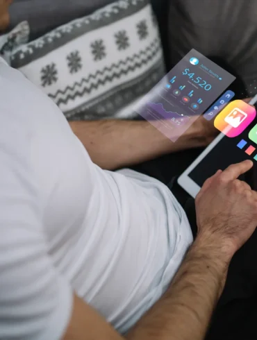 A person in a white shirt uses a tablet displaying holographic financial graphs and app icons, conveying a futuristic and tech-savvy atmosphere.