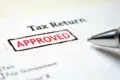 Close-up of a tax return document with a red "Approved" stamp. A pen lies nearby, conveying a sense of completion and approval.