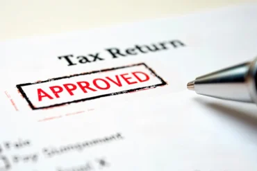 Close-up of a tax return document with a red "Approved" stamp. A pen lies nearby, conveying a sense of completion and approval.