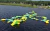 A large inflatable water park floats on a lake, featuring slides, obstacles, and climbing structures in green and yellow. People play under a clear sky.