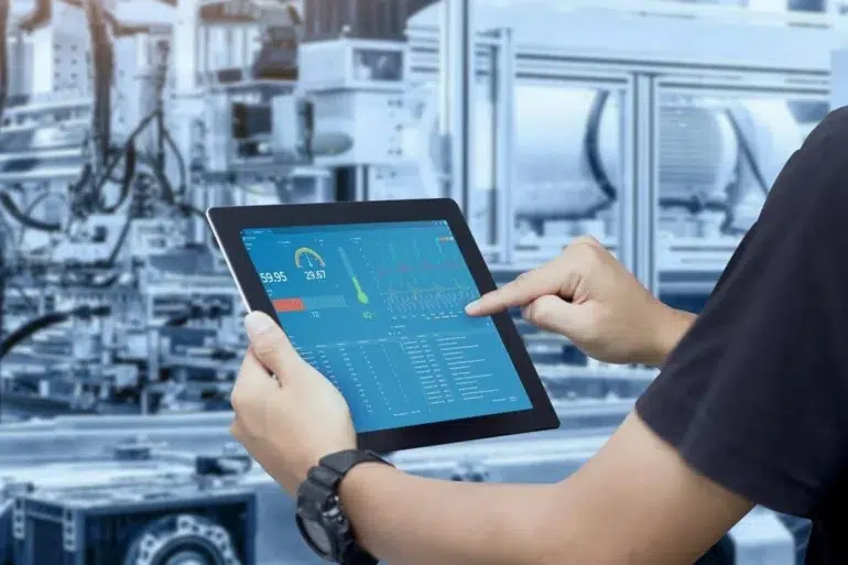 A person interacts with a tablet displaying industrial data and metrics, set against a background of machinery in a factory environment.