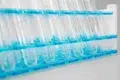 Clear empty test tubes held in a blue plastic rack, arranged in rows on a white surface in a laboratory setting.