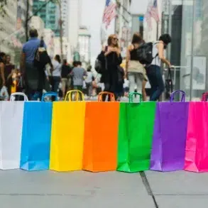 A row of colorful shopping bags in blue, yellow, orange, green, purple, and pink lined up on a busy city street.