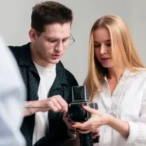 Two individuals are engaged in a photography discussion, examining a vintage camera in a well-lit studio setting.