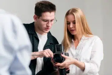 Two individuals are engaged in a photography discussion, examining a vintage camera in a well-lit studio setting.