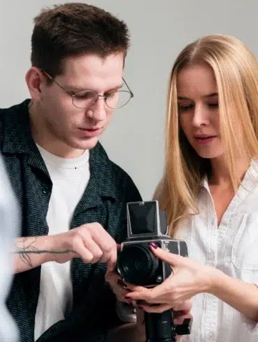 Two individuals are engaged in a photography discussion, examining a vintage camera in a well-lit studio setting.