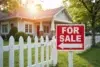 Cozy house with white picket fence for sale, sign in foreground. Sunlight filters through trees, creating a warm, inviting atmosphere.