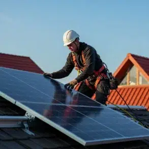 A worker in a safety harness installs solar panels on a tiled roof under a clear blue sky. The scene conveys efficiency and sustainable energy.