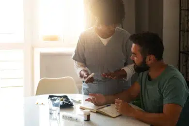 A healthcare provider discusses medication and treatment with a patient at a bright table, surrounded by medical supplies and a notebook.