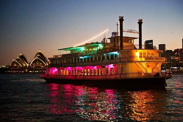 An elegant Sydney Harbour dinner cruise vessel sailing past the illuminated Opera House.
