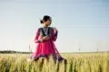 A woman in a vibrant pink and blue traditional dress stands gracefully in a golden wheat field under a clear sky, exuding a serene and elegant aura.