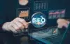 A person holds a magnifying glass revealing "SEO" amidst glowing digital graphs and charts, conveying data analysis and a focus on search engine optimization.