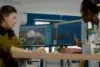 Two women collaborate at a desk with dual monitors displaying 3D design software. The setting is a modern office, with a focused, creative atmosphere.