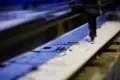 A CNC laser cutter precisely etches intricate designs onto a flat metal sheet in a workshop, reflecting a focus on precision and technology.