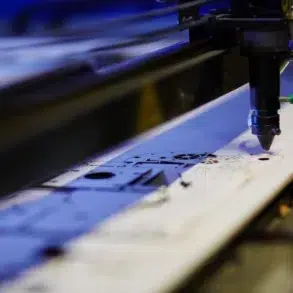 A CNC laser cutter precisely etches intricate designs onto a flat metal sheet in a workshop, reflecting a focus on precision and technology.