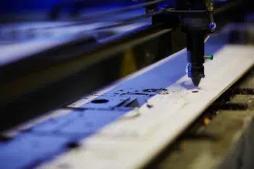 A CNC laser cutter precisely etches intricate designs onto a flat metal sheet in a workshop, reflecting a focus on precision and technology.