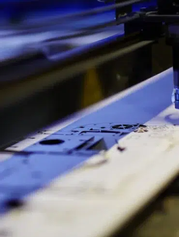 A CNC laser cutter precisely etches intricate designs onto a flat metal sheet in a workshop, reflecting a focus on precision and technology.