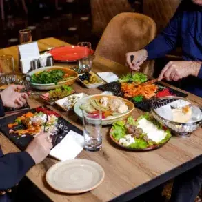 Two people dining at a wooden table, enjoying a variety of colorful dishes, including salads, olives, and appetizers, creating a lively, cozy atmosphere.