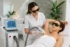 Woman receiving laser hair removal treatment on her underarm by a technician in a spa-like clinic setting.
