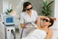 Woman receiving laser hair removal treatment on her underarm by a technician in a spa-like clinic setting.