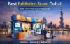 A modern exhibition stand with people interacting, set against a Dubai skyline at sunset.