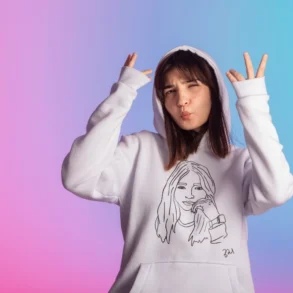 Young woman in a white hoodie adorned with a line drawing poses playfully against a pink and blue gradient background, expressing a cheerful vibe.