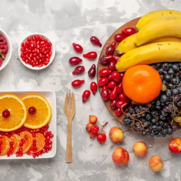 Assortment of colorful fruits on a marble surface. Bananas, orange, grapes, and apples on a wooden plate. Sliced oranges, raspberries, and pomegranate in bowls. Festive and fresh.