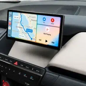 Car dashboard with a digital display showing navigation map and music controls. The map highlights a route near San Mateo. Buttons below are for climate control.