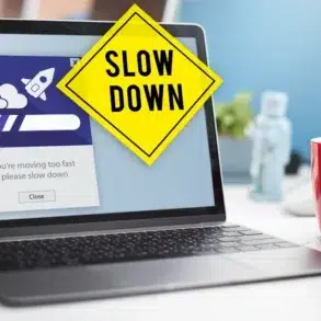 A laptop displays a progress bar with a rocket icon, overlaid by a yellow "Slow Down" sign. A red mug with "7" sits nearby, suggesting a cautionary tone.