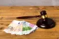 A judge's gavel rests beside a stack of Euro banknotes on a wooden table, symbolizing legal and financial matters with a serious tone.