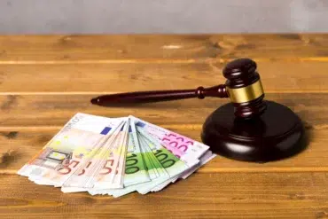 A judge's gavel rests beside a stack of Euro banknotes on a wooden table, symbolizing legal and financial matters with a serious tone.