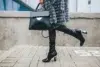 Fashionable person in a fur coat carries a black handbag and wears sheer polka-dot tights with glossy black boots, exuding chic style.