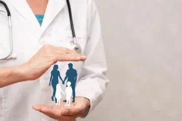 A doctor with a stethoscope holds an illustrated family silhouette, symbolizing healthcare. The image conveys protection and care in a soft, reassuring tone.