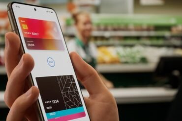 Person holding smartphone with digital wallet app displaying two credit cards in a grocery store checkout setting.